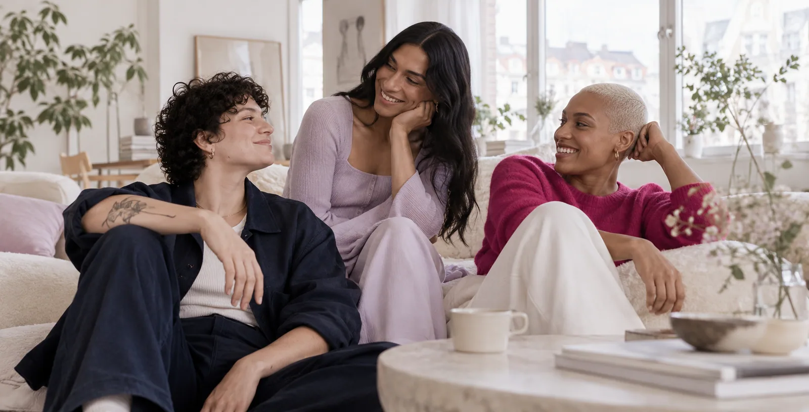 Drei genderdiverse Erwachsene in einem hellen Raum im entspannten Gespräch
